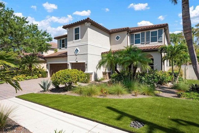 mediterranean / spanish home featuring a front yard, stucco siding, decorative driveway, a tiled roof, and an attached garage