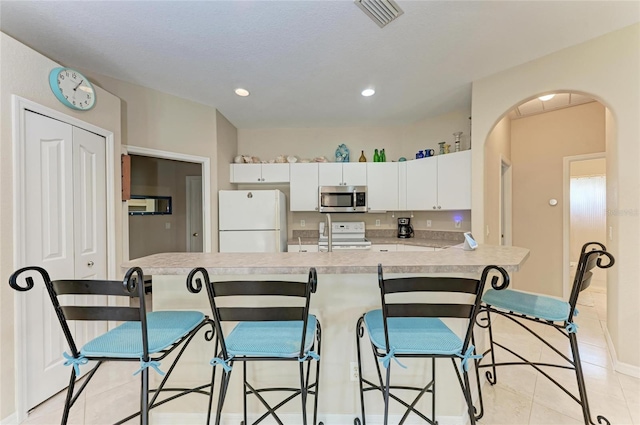 1631 Madison Ave, North Port, FL 34286 - kitchen with visible vents, arched walkways, white appliances, a kitchen bar, and white cabinetry