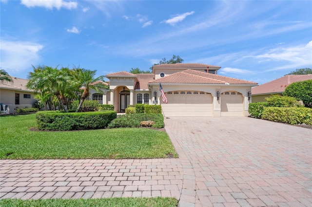 mediterranean / spanish home with a tile roof, a front yard, stucco siding, decorative driveway, and an attached garage