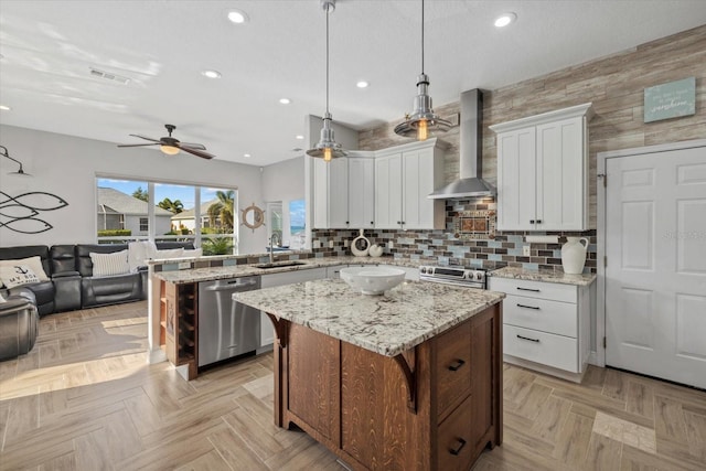 kitchen with a peninsula, wall chimney range hood, a sink, stainless steel appliances, and open floor plan