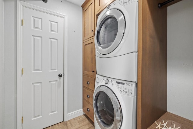 washroom featuring stacked washer / drying machine, baseboards, and cabinet space