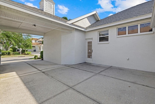 exterior space with roof with shingles, a chimney, a patio area, and stucco siding