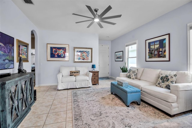 living area featuring a ceiling fan, arched walkways, light tile patterned floors, and baseboards