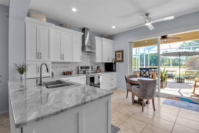kitchen featuring wall chimney range hood, electric range, a sink, a sunroom, and white cabinetry