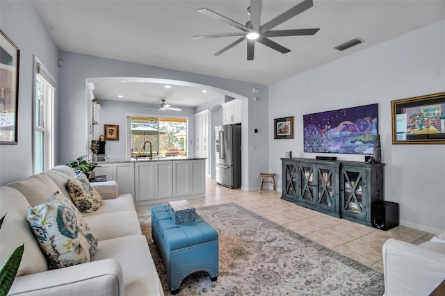 living area with ceiling fan, arched walkways, light tile patterned floors, and baseboards