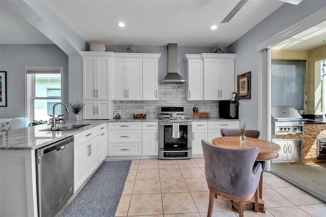 kitchen featuring stainless steel appliances, wall chimney range hood, a sink, decorative backsplash, and white cabinets