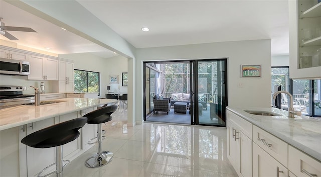 5324 Siesta Ct, Sarasota, FL 34242 - kitchen featuring a sink, appliances with stainless steel finishes, a breakfast bar, white cabinetry, and light stone counters