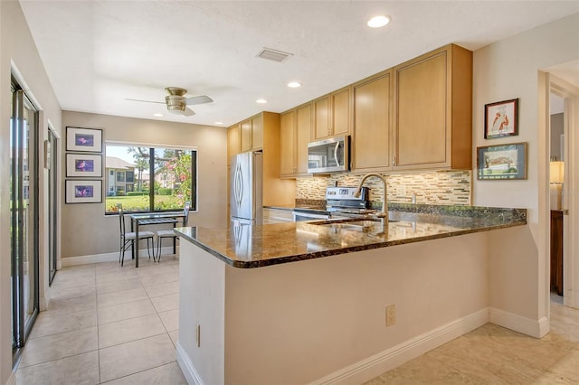 kitchen with tasteful backsplash, baseboards, dark stone countertops, appliances with stainless steel finishes, and a sink