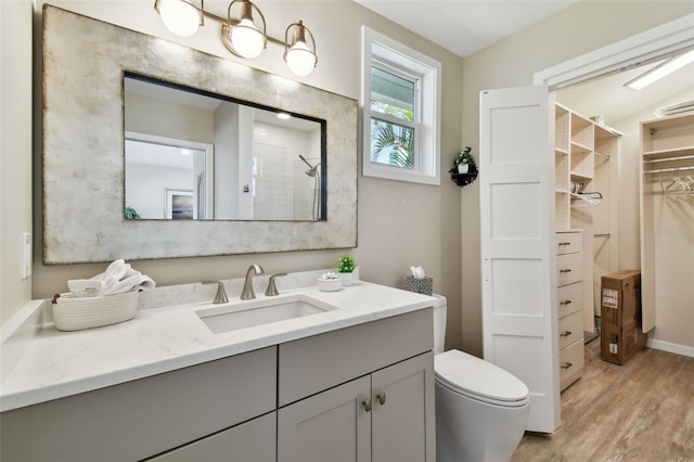 bathroom featuring a tile shower, wood finished floors, toilet, vanity, and a walk in closet