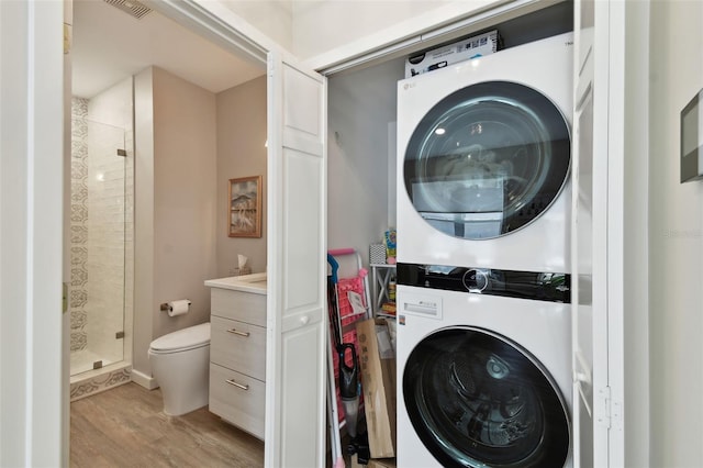 washroom featuring stacked washer / drying machine, light wood-style flooring, visible vents, and laundry area