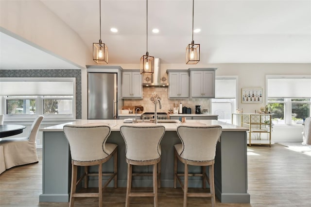 kitchen with tasteful backsplash, a center island with sink, freestanding refrigerator, gray cabinetry, and light countertops