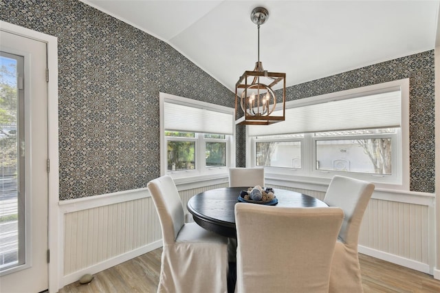 dining area with wallpapered walls, vaulted ceiling, wood finished floors, and a chandelier