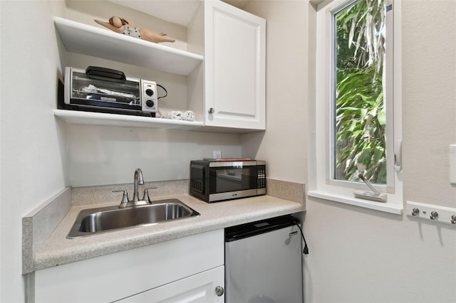 kitchen featuring open shelves, a sink, light countertops, stainless steel microwave, and white cabinetry