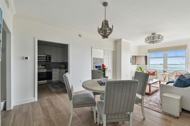 dining space with an inviting chandelier, a water view, light wood-style floors, crown molding, and a textured ceiling
