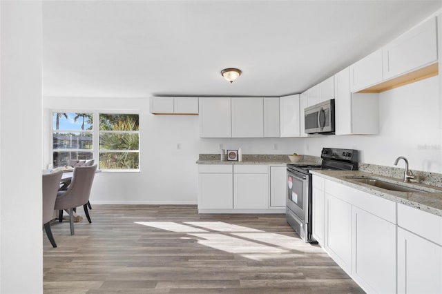 221 Duxbury Ave, Port Charlotte, FL 33952 - kitchen with light wood-type flooring, a sink, light stone counters, stainless steel appliances, and white cabinetry