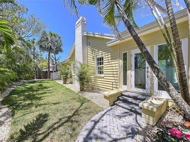 view of property exterior with entry steps, a chimney, and a lawn