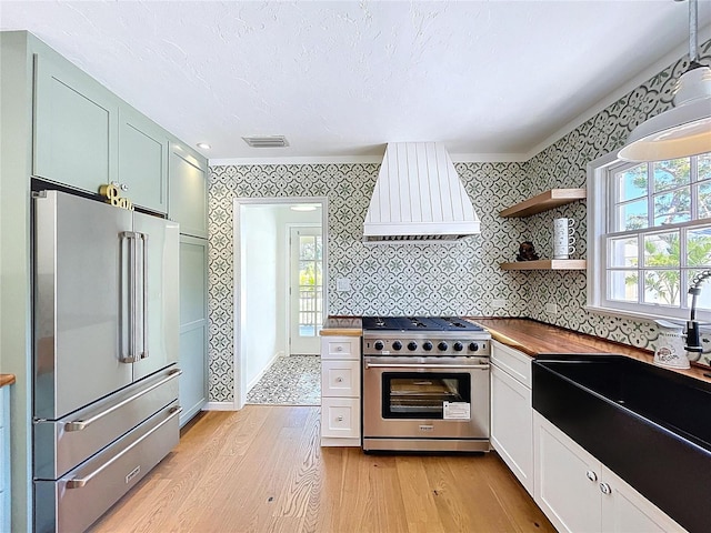 kitchen with plenty of natural light, premium range hood, high end appliances, light wood finished floors, and wallpapered walls