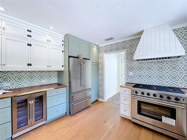 kitchen featuring light wood-type flooring, ventilation hood, wine cooler, butcher block countertops, and premium appliances
