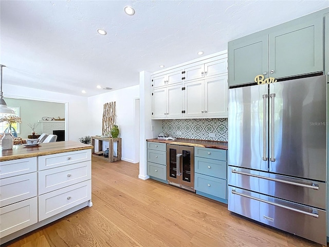 kitchen with high end fridge, white cabinets, light wood-style floors, decorative backsplash, and beverage cooler