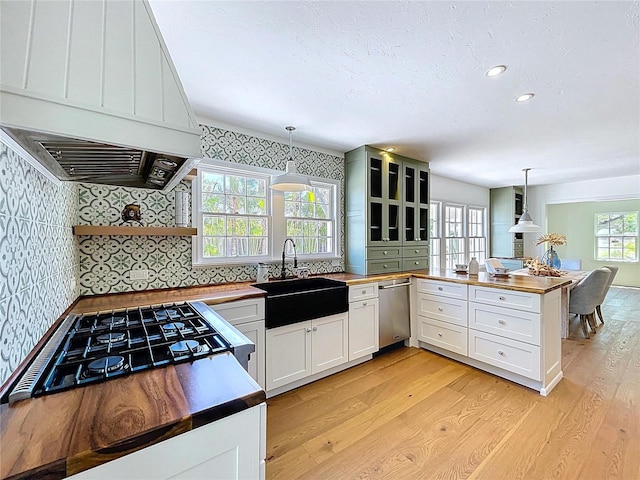 kitchen featuring exhaust hood, a sink, light wood-type flooring, a peninsula, and butcher block counters