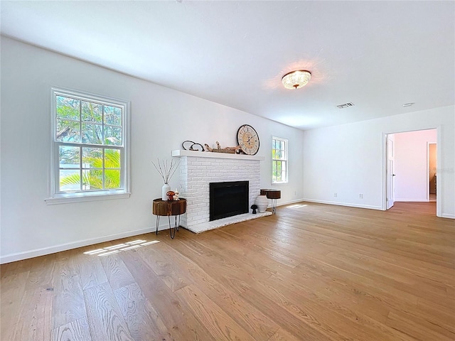 living room featuring visible vents, baseboards, a brick fireplace, and light wood-style floors