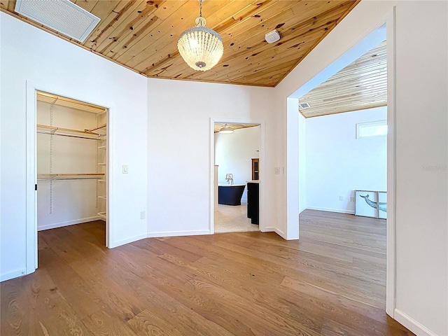 unfurnished bedroom with a walk in closet, wood ceiling, wood finished floors, and visible vents