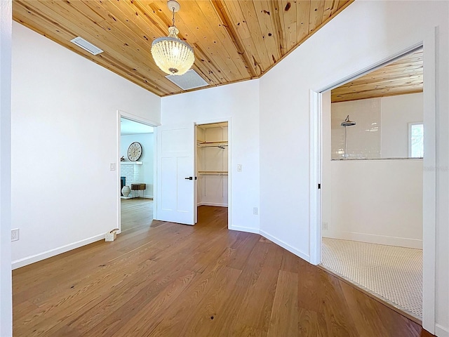 unfurnished bedroom with visible vents, baseboards, wooden ceiling, a walk in closet, and wood finished floors
