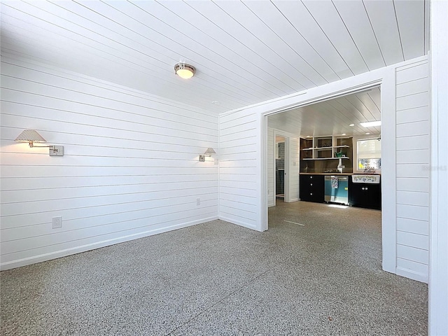 empty room with wooden ceiling, wood walls, baseboards, and speckled floor