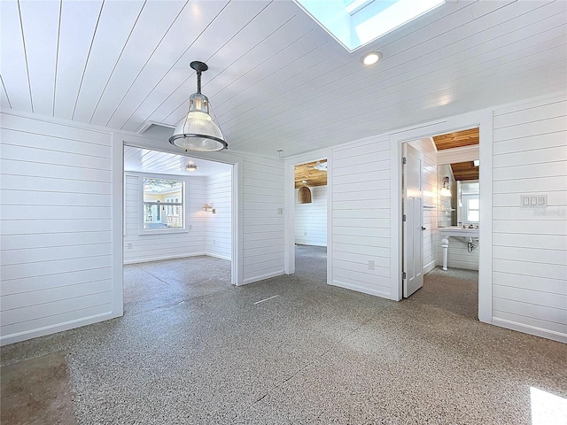 unfurnished dining area featuring a skylight, wooden walls, speckled floor, and a wealth of natural light