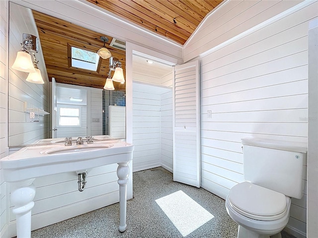 bathroom featuring wooden ceiling, toilet, wood walls, lofted ceiling with skylight, and a sink
