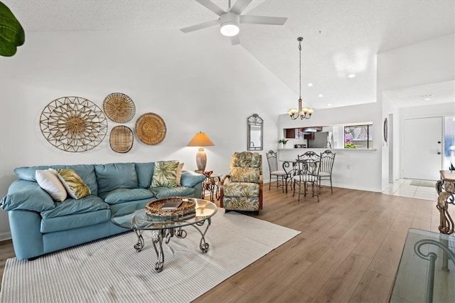 living area with ceiling fan with notable chandelier, wood finished floors, baseboards, and high vaulted ceiling