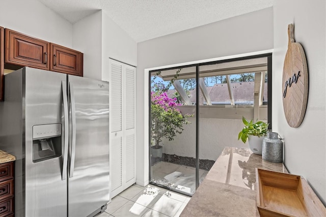 kitchen with light tile patterned flooring, a textured ceiling, light stone counters, and stainless steel fridge with ice dispenser