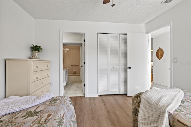 bedroom with a closet, ensuite bathroom, a textured ceiling, visible vents, and light wood-style floors