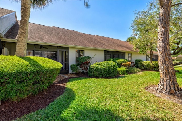 ranch-style house with roof with shingles, ceiling fan, stucco siding, and a front lawn