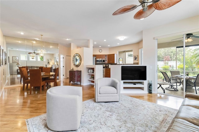 living area with a wealth of natural light, ceiling fan with notable chandelier, and light wood-style floors