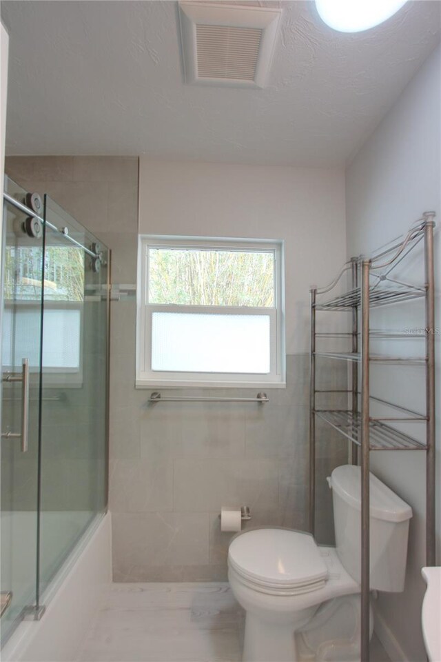 306 Island Cir, Sarasota, FL 34242 - full bath with visible vents, toilet, tile walls, and shower / bath combination with glass door