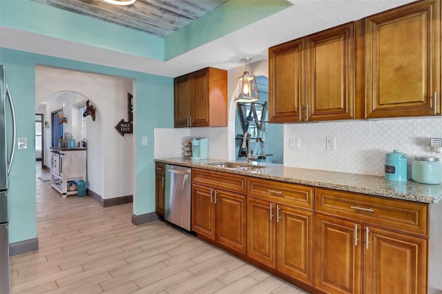 23088 Allen Ave, Port Charlotte, FL 33980 - kitchen featuring appliances with stainless steel finishes, arched walkways, brown cabinetry, light stone countertops, and tasteful backsplash