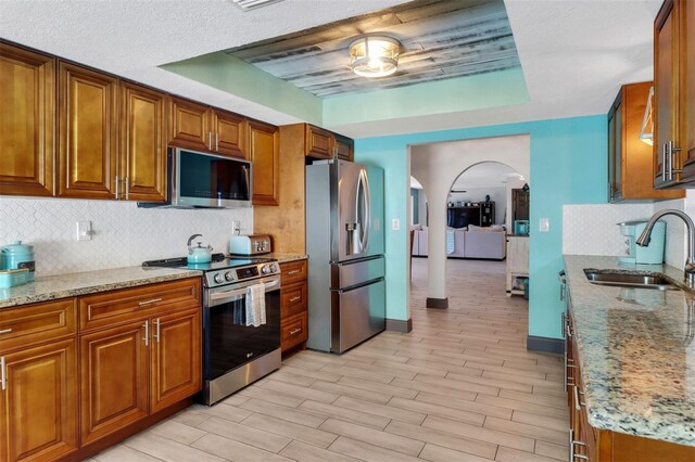 23088 Allen Ave, Port Charlotte, FL 33980 - kitchen with appliances with stainless steel finishes, arched walkways, brown cabinetry, decorative backsplash, and light stone counters