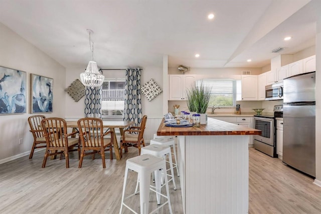 kitchen with light wood-style flooring, butcher block counters, a breakfast bar area, and stainless steel appliances