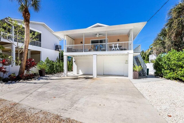 raised beach house featuring concrete driveway, stairs, ceiling fan, a garage, and covered porch