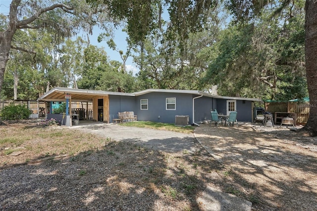rear view of property with cooling unit, a carport, fence, stucco siding, and view of scattered trees