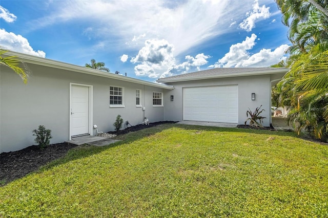 back of property with a yard, a garage, stucco siding, and driveway