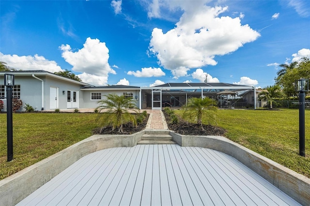 rear view of property with french doors, stucco siding, a lanai, and a lawn
