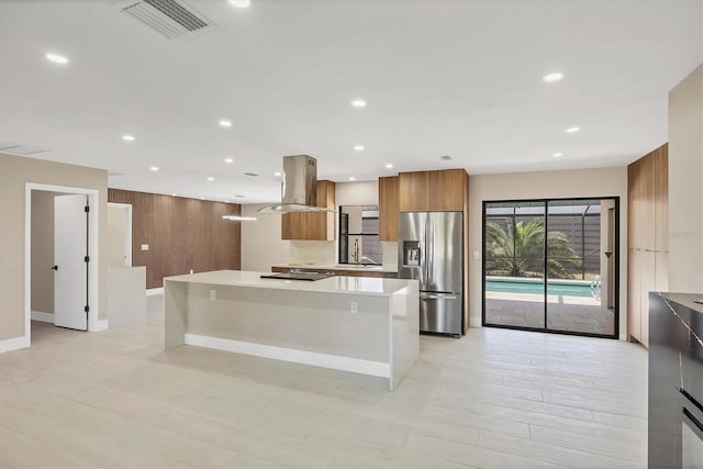 kitchen with island exhaust hood, stainless steel fridge, modern cabinets, brown cabinetry, and light countertops