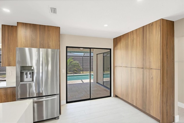 kitchen with brown cabinets, modern cabinets, light countertops, stainless steel refrigerator with ice dispenser, and recessed lighting