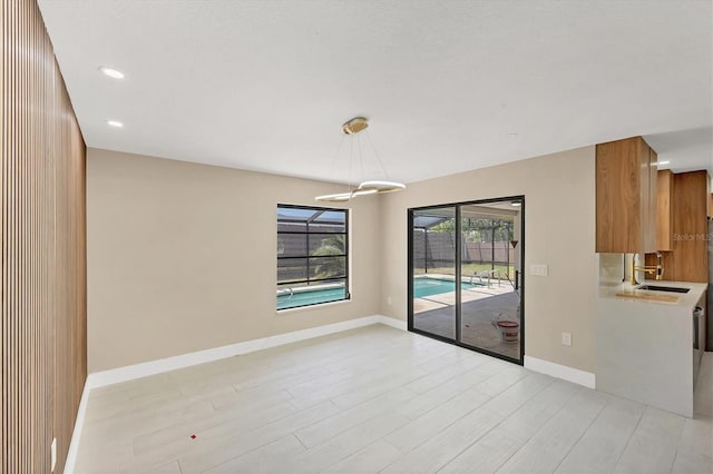 unfurnished dining area with recessed lighting, light wood-type flooring, baseboards, and a sink