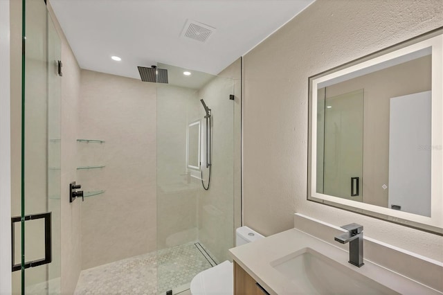 bathroom featuring tiled shower, vanity, a textured wall, toilet, and recessed lighting