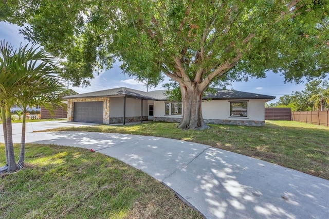 ranch-style house featuring driveway, stone siding, fence, an attached garage, and a front yard