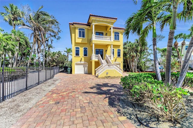 raised beach house with a balcony, stucco siding, stairs, a tiled roof, and fence
