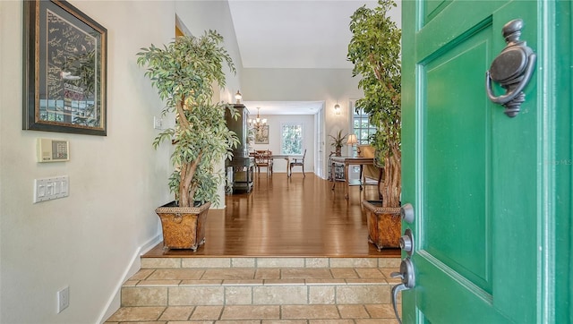 foyer entrance featuring baseboards, stone tile flooring, and an inviting chandelier